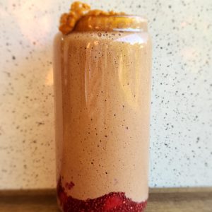 Peanut butter smoothie in a tall glass with homemade jam on the bottom and cacao and peanut butter dolloped on top.