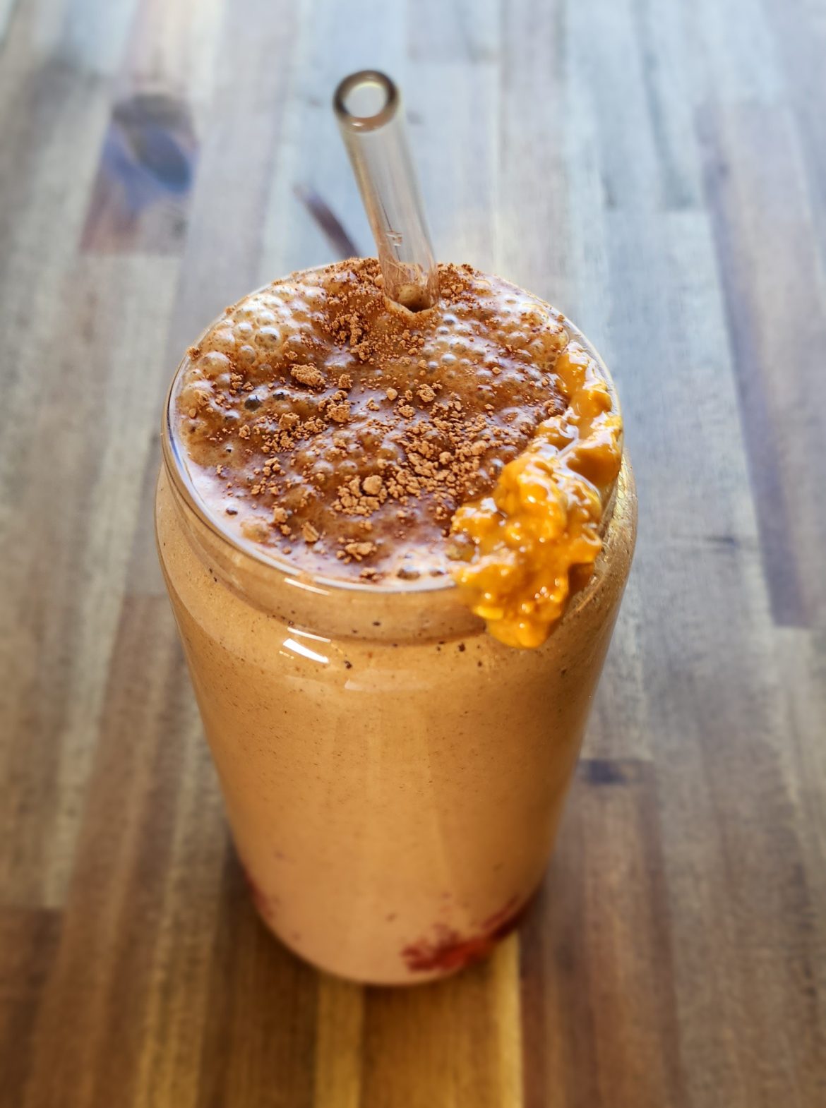 Peanut butter smoothie in a tall glass with homemade jam on the bottom and cacao and peanut butter dolloped on top.